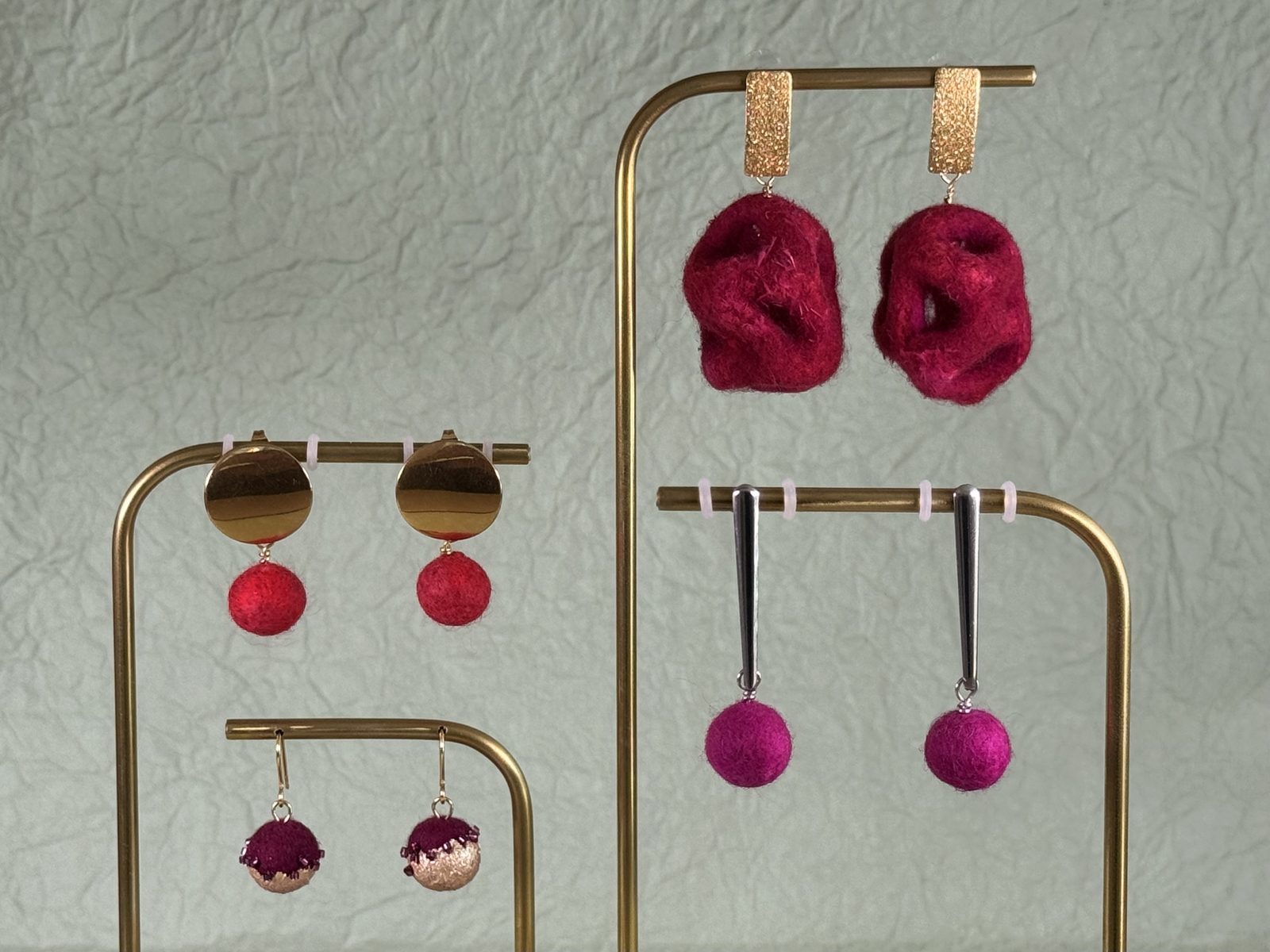 Mehrere Paar handgefilzte Ohrringe mit Anhaengern in Rot und Magenta auf goldenen Staendern
